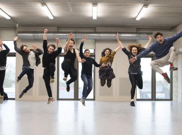 Nine students in a row jumping excitedly in a brightly lit new studio