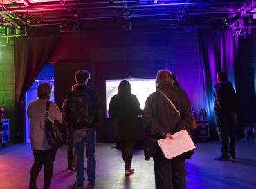 Seven adult members of the public looking at a screen in a colourfully lit studio