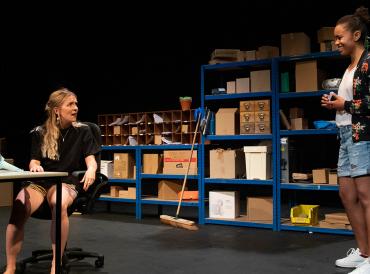 Two LAMDA graduating students in casual clothes in dialogue, with shelves in the background