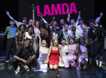 Photo of graduating LAMDA students smiling and cheering at the farewell celebration