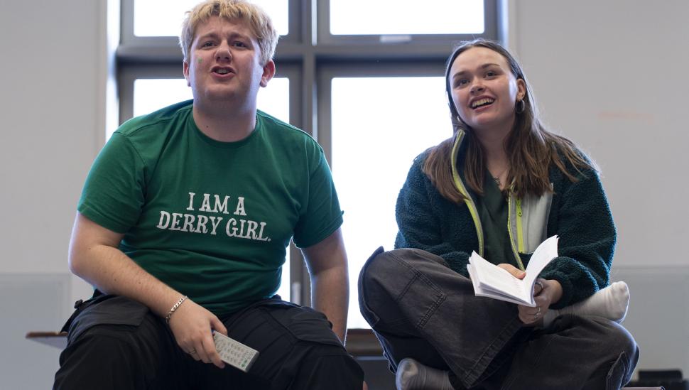 Students smiling and holding scripts in rehearsal